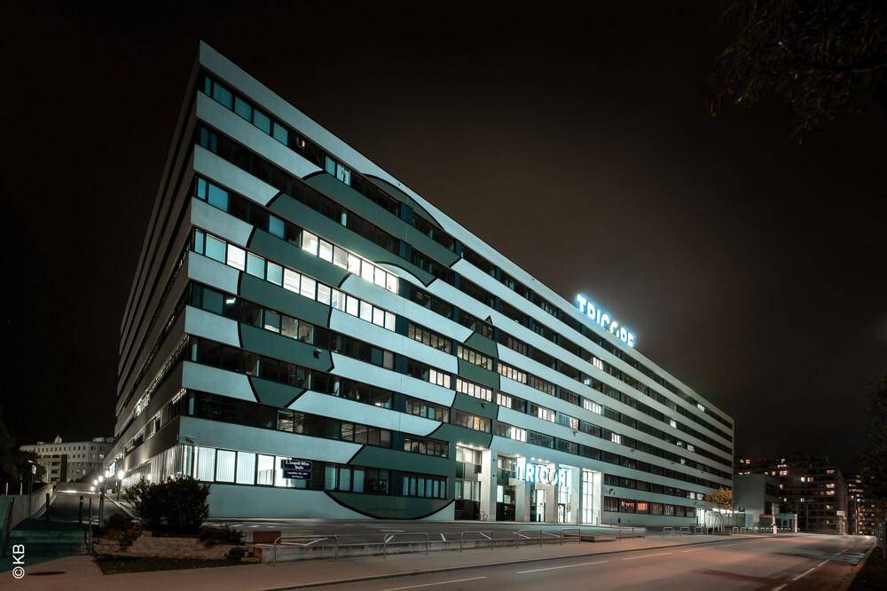 Das moderne Bürogebäude bei Nacht, mit beleuchteter Fassade und Fenstern, die Licht ausstrahlen.