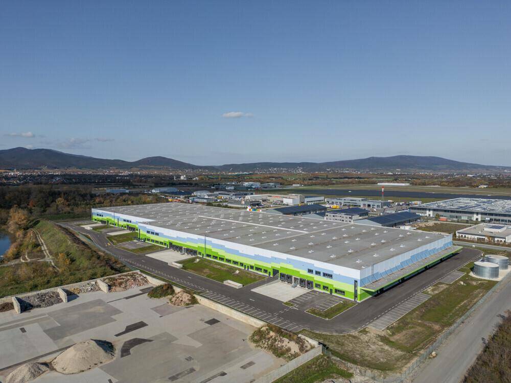 Weitläufige Ansicht des Logistikzentrums mit angrenzenden Feldern und weiteren Industriegebäuden in der Ferne.