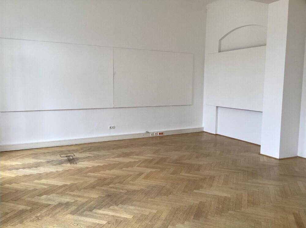 Geräumiges Zimmer mit Fischgrätparkett, weißen Wänden und einer Nische mit Bogen.