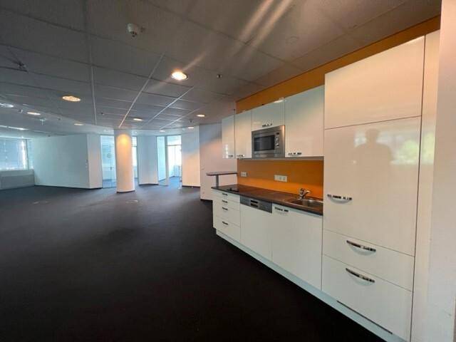 Moderne Küchenzeile mit weißen Hochglanzschränken, Mikrowelle und orangefarbener Rückwand in einem Bürobereich.
