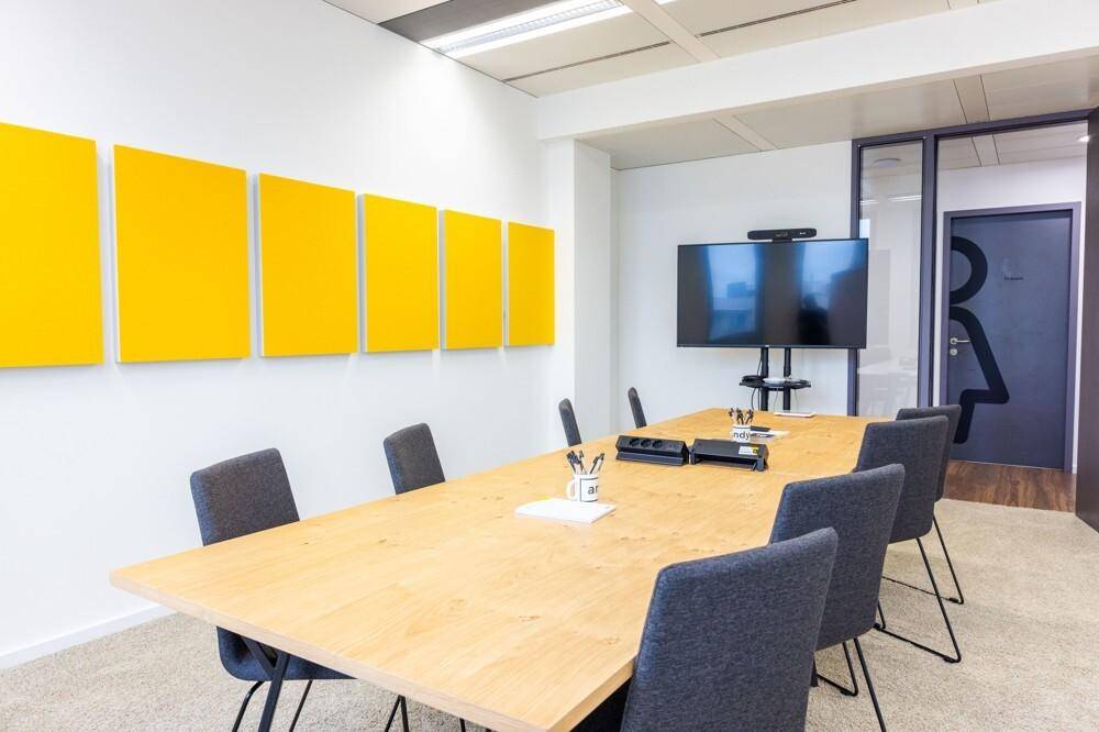 Konferenzraum mit großem Holztisch, bequemen Stühlen und einem Wandfernseher für Präsentationen.