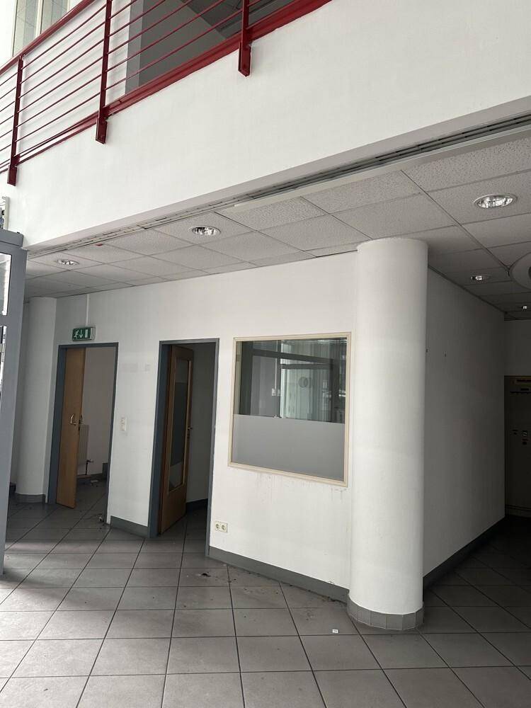 Empfangsbereich oder Flur in einem Bürogebäude mit gefliestem Boden und einer roten Balustrade im Obergeschoss.