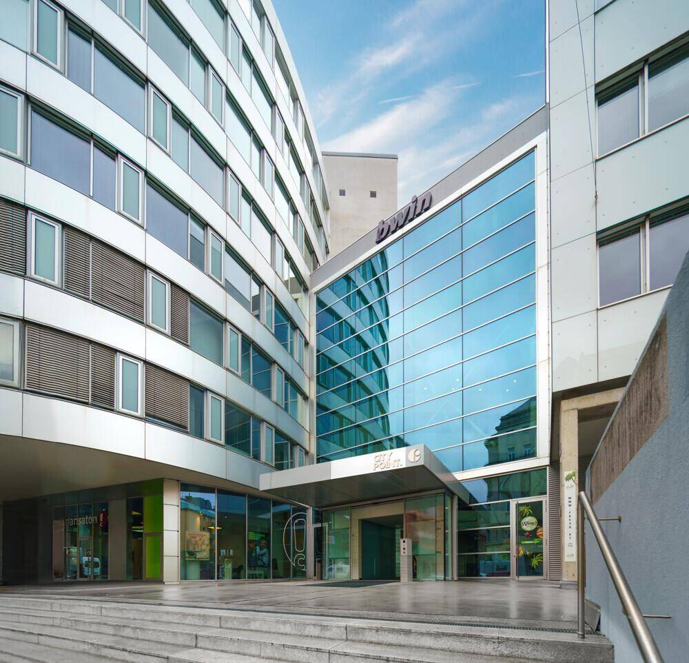 Eingangsbereich eines modernen Bürogebäudes mit beeindruckender Glasfassade und breiter Treppe.
