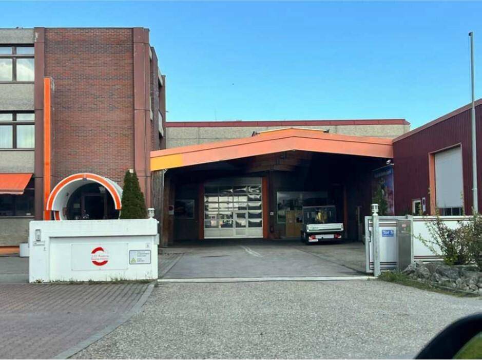 Eingangsbereich eines Gebäudes mit Ziegelfassade, überdachter Zufahrt und einem Garagentor, dahinter ein Fahrzeug.