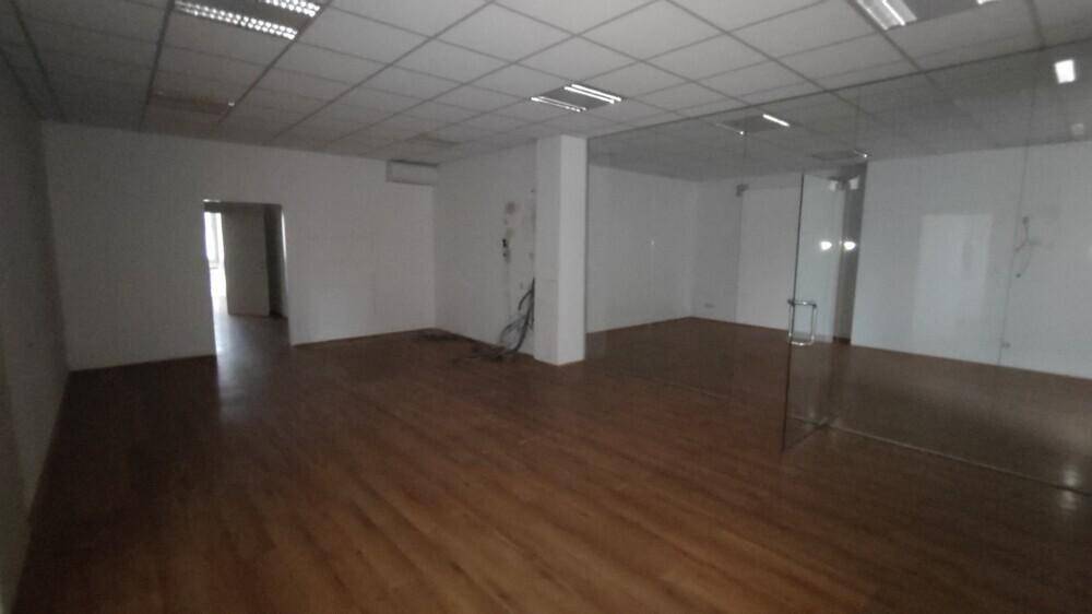 Offener Bürobereich mit Holzboden, Rasterdecke und einer Glastür, die zu einem weiteren Raum führt.