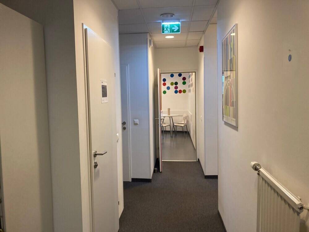 Heller Flur mit weißen Türen und Teppichboden, der zu weiteren Büroräumen führt.