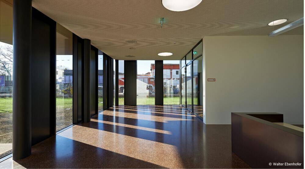 Heller Flur mit großen Glasfronten, die den Blick nach draußen freigeben und viel Sonnenlicht hereinlassen.