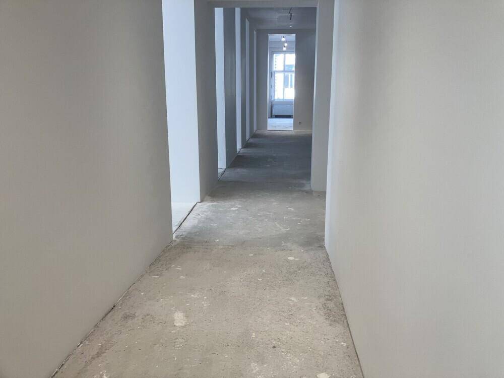 Langer, heller Flur mit weißen Wänden und einem Betonboden, der auf den Endausbau wartet.
