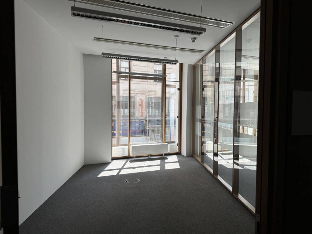 Helles Büro mit Teppichboden, großen Fenstern und Blick auf die Stadt, ideal für konzentriertes Arbeiten.