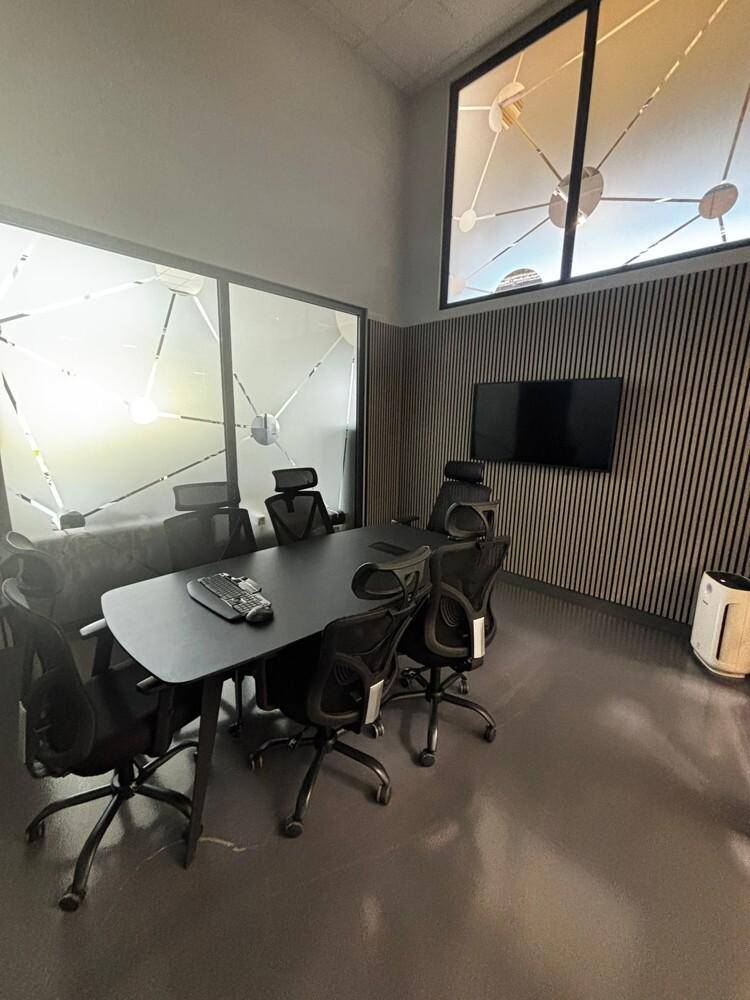 Konferenzraum mit großem Tisch, ergonomischen Stühlen, Wandfernseher und schallabsorbierenden Holzpaneelen.