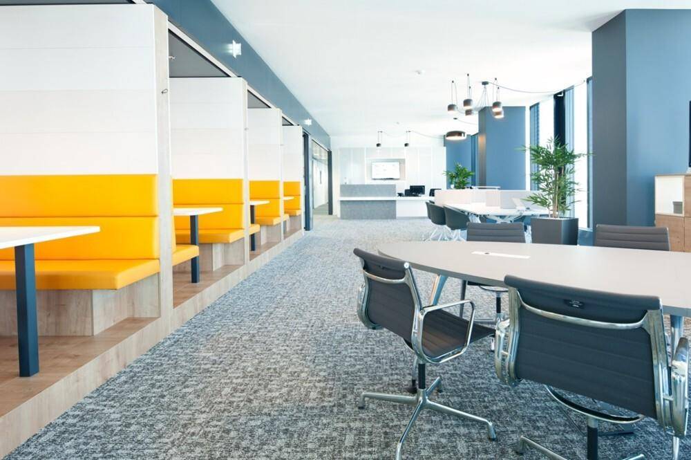 Offener Bürobereich mit orangefarbenen Sitzkabinen und modernen Tischen, ideal für kollaboratives Arbeiten.