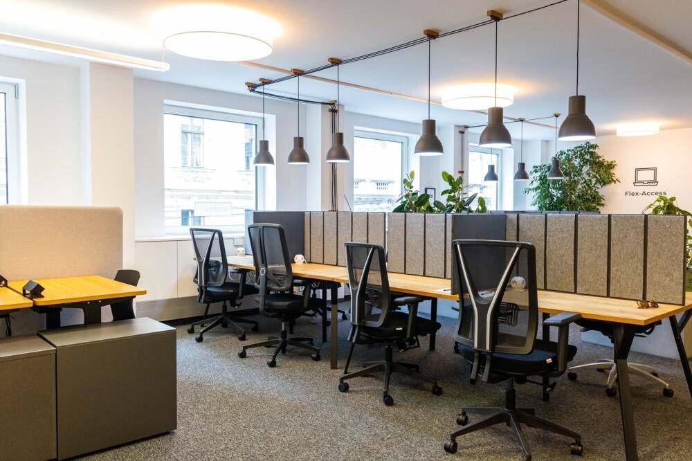 Großraumbüro mit mehreren Arbeitsplätzen, ergonomischen Stühlen, Akustikpaneelen und Hängeleuchten.