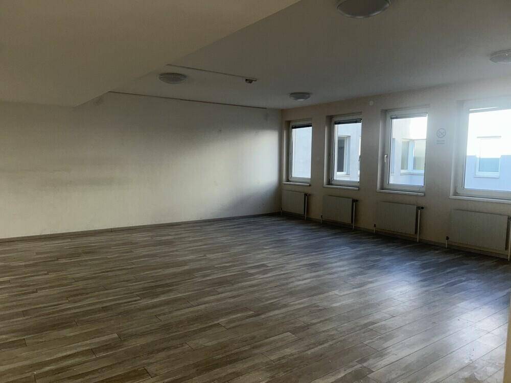 Heller Büroraum mit großen Fenstern, Heizkörpern und einem Boden in Holzoptik.
