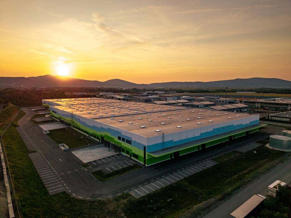 Sonnenuntergang über einem großen Logistikzentrum mit farbiger Fassade und weitem Blick auf die Umgebung.