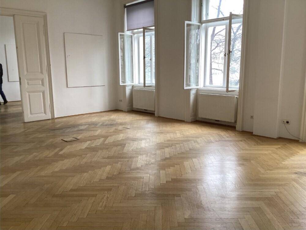 Großes Zimmer mit Fischgrätparkett, hohen Fenstern und viel natürlichem Licht.