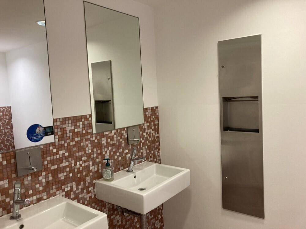Heller Waschraum mit zwei modernen Waschbecken, großen Spiegeln und braunen Mosaikfliesen.
