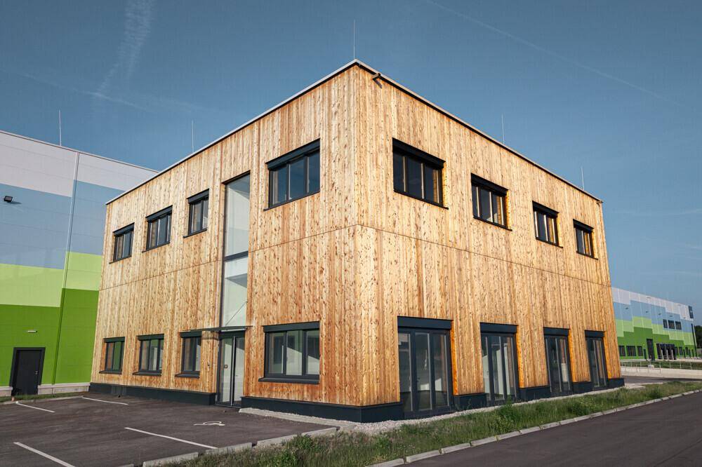 Modernes Bürogebäude mit Holzfassade und großen Fenstern, umgeben von Grünflächen.