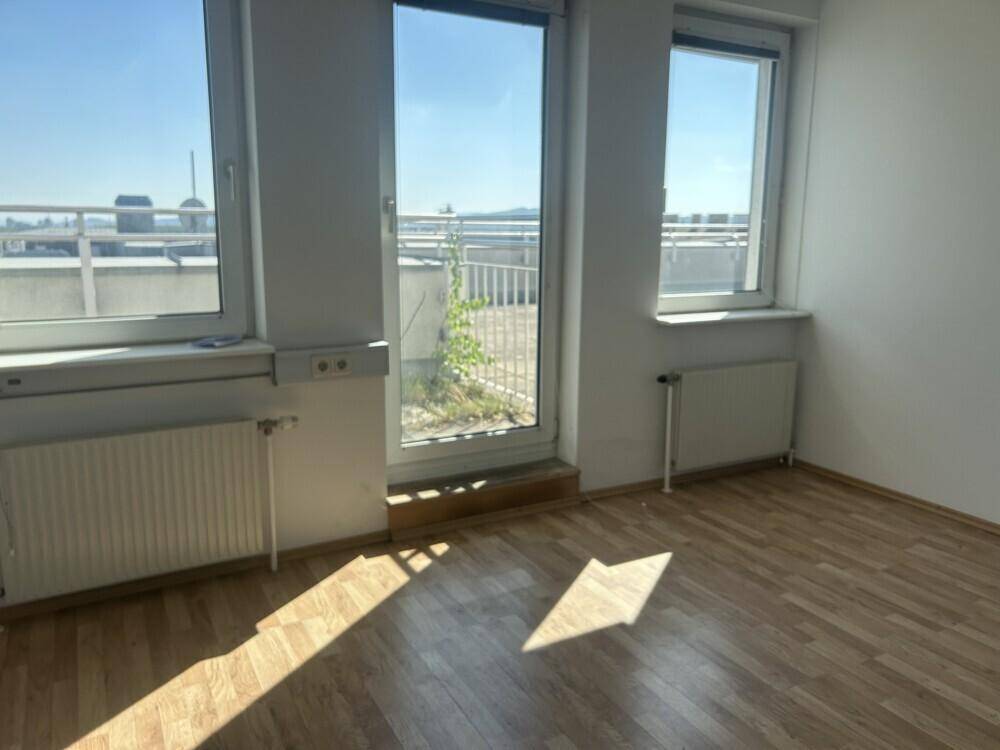 Heller Büroraum mit Laminatboden und Zugang zu einer Außenterrasse durch eine Glastür.