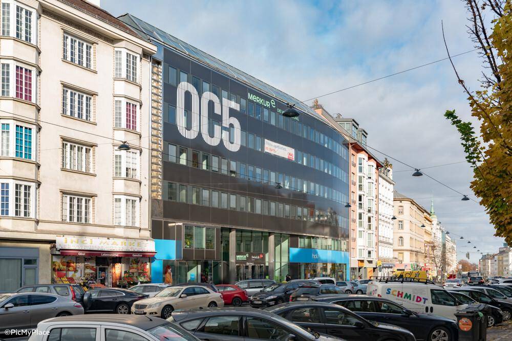 Ansicht des modernen Bürogebäudes OC5 von der Straße aus mit parkenden Autos.