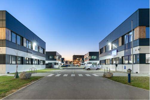 Blick auf einen modernen Industriepark mit mehreren Gebäuden, Straße und Parkplätzen bei Dämmerung.