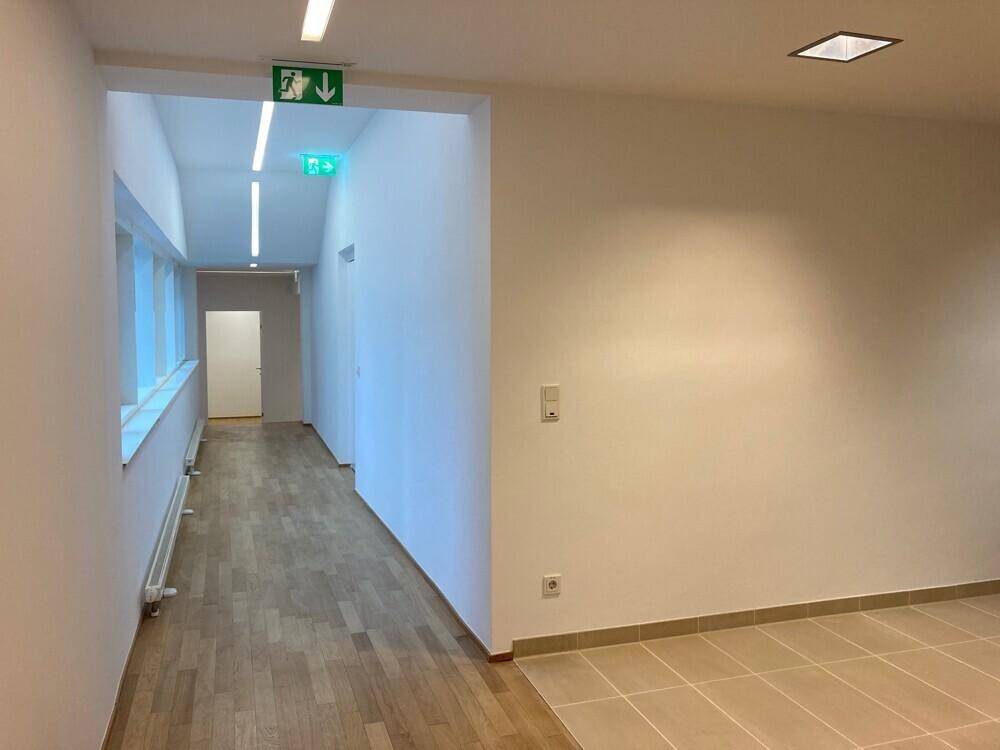 Heller Bürobereich mit Fliesenboden, Fenstern und einem langen Flur mit Holzboden.