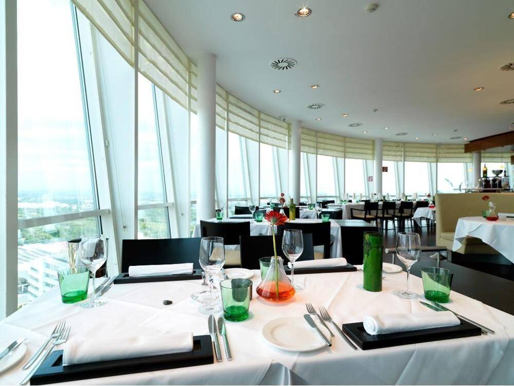 Elegantes Restaurant mit Panoramablick durch große, geschwungene Fenster und gedeckten Tischen.