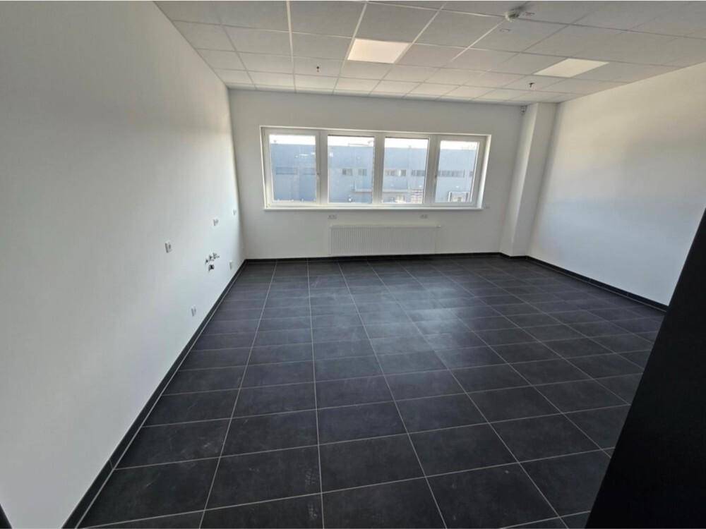 Leerer Raum mit dunklem Fliesenboden, weißen Wänden und einer Fensterfront, die den Blick nach draußen freigibt.