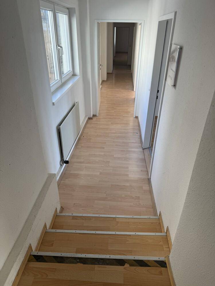 Langer Flur mit Laminatboden, hellen Wänden und Fenstern, der zu weiteren Räumen führt.