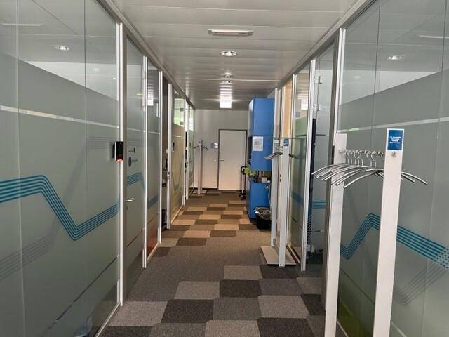 Langer Büroflur mit Glaswänden zu den einzelnen Büros und gemustertem Teppichboden.