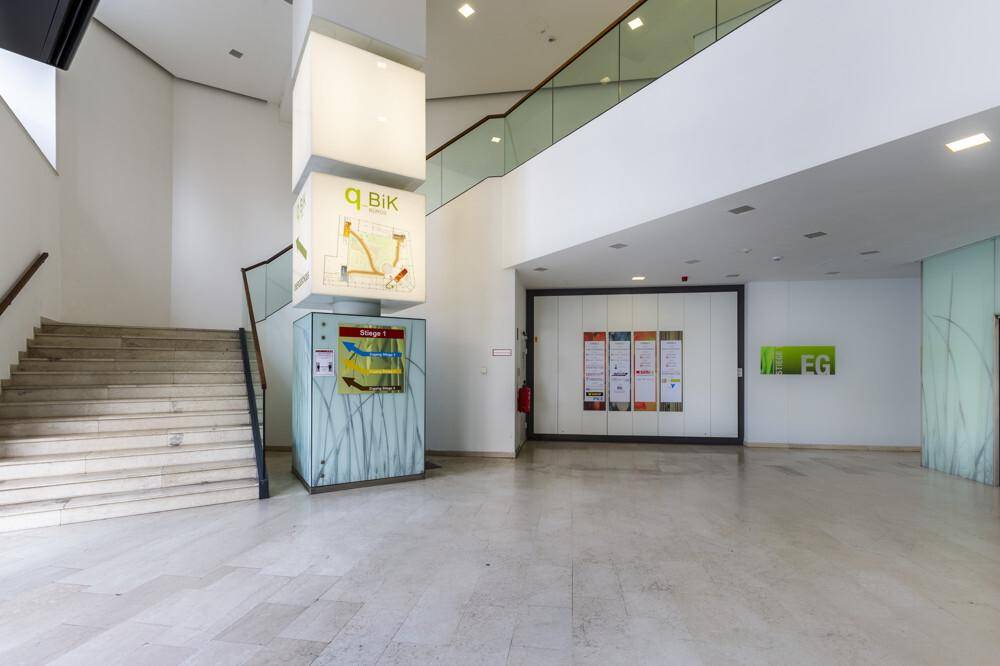 Geräumiger Empfangsbereich mit einer breiten Treppe, Informationsdisplays und Zugang zu den oberen Etagen.
