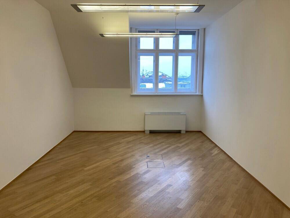 Geräumiges Büro mit Holzboden, Dachschräge und einem großen Fenster, das viel Tageslicht spendet.