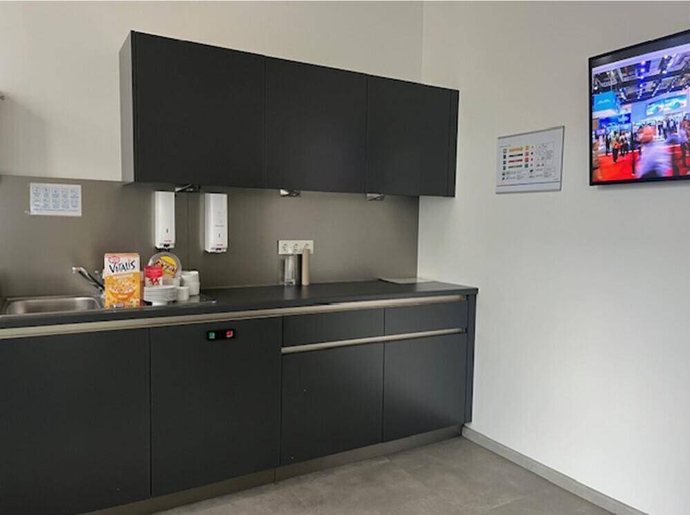 Moderne Küchenzeile mit dunklen Schränken, Spüle und einem Fernseher an der Wand.