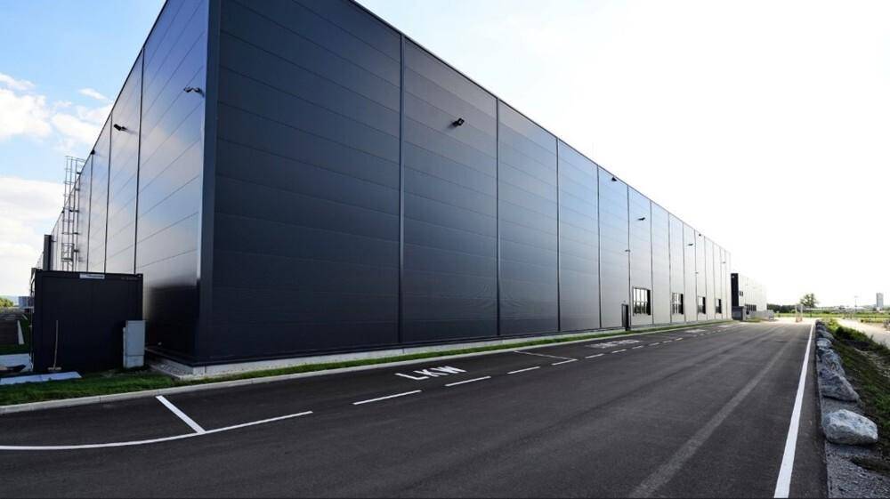 Seitenansicht der großen Logistikhalle mit dunkler Fassade und Zufahrtsstraße.