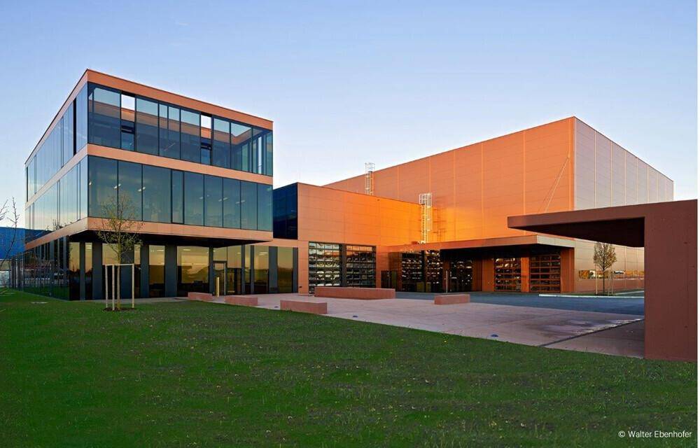 Architektonisch ansprechendes Geschäftsgebäude bei Sonnenuntergang mit weitläufiger Rasenfläche und Eingangsbereich.