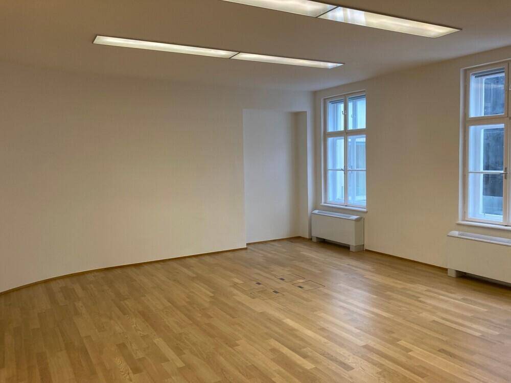 Weitläufiges Büro mit Holzboden, abgerundeter Wand und moderner Deckenbeleuchtung.