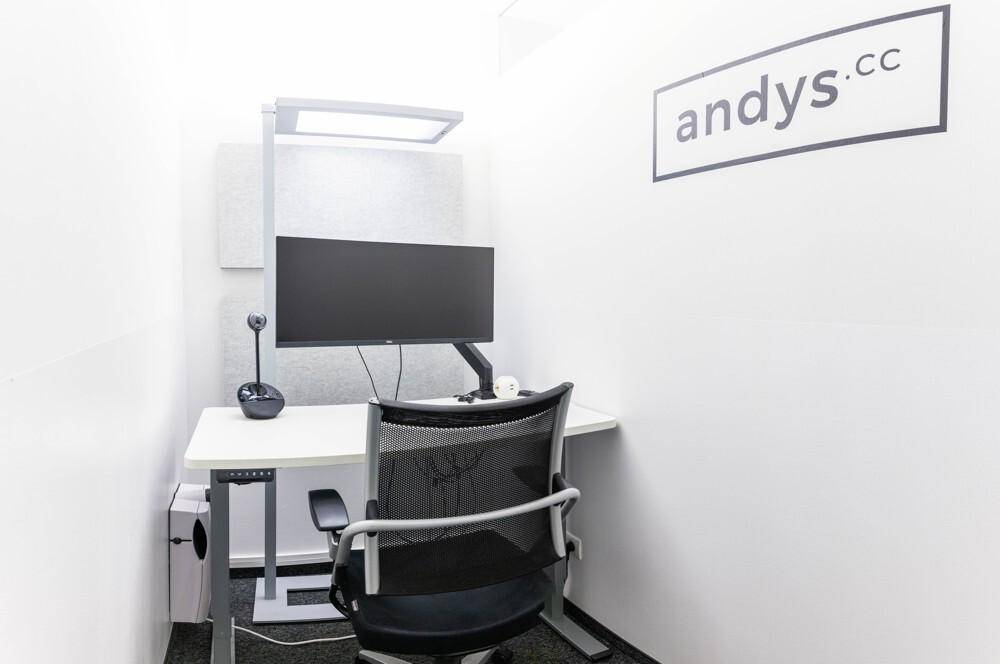 Kleiner, privater Arbeitsbereich oder Telefonzelle mit Schreibtisch, Monitor und ergonomischem Bürostuhl.