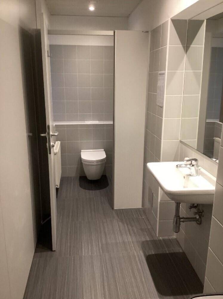 Modernes Badezimmer mit grauen Fliesen, wandhängendem WC und Waschbecken.