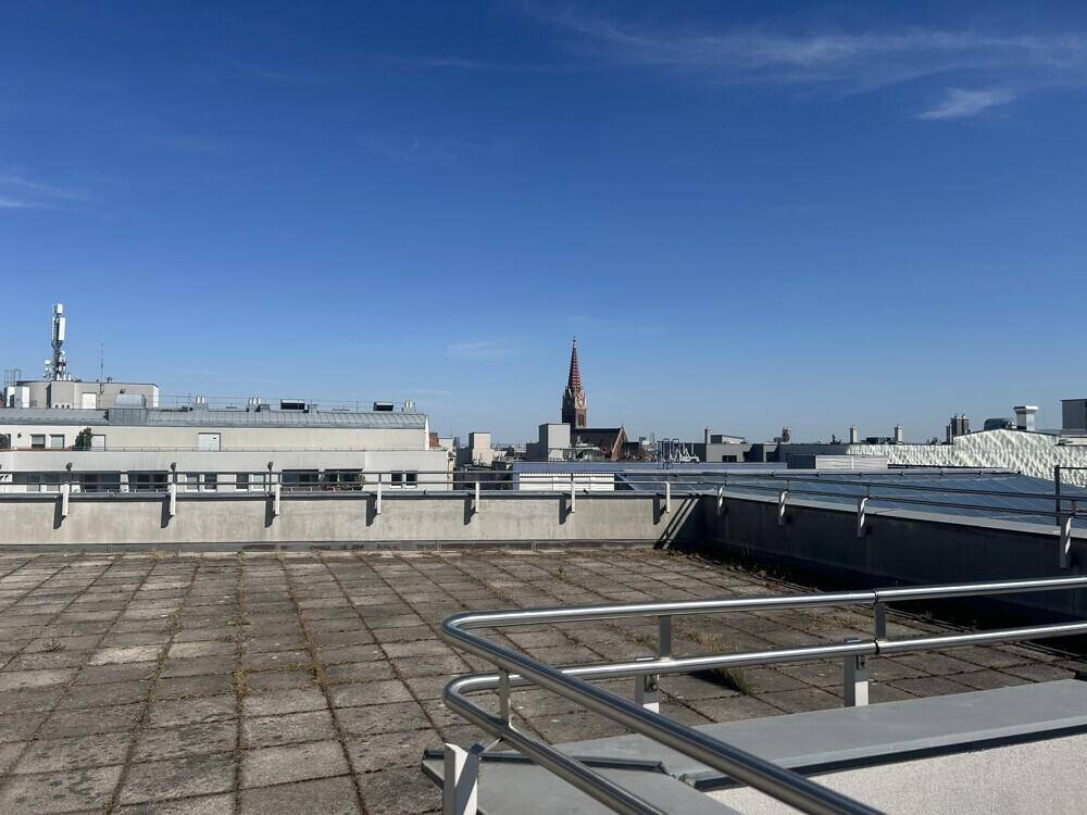 Große Dachterrasse mit weitem Blick über die Stadt und einem Kirchturm am Horizont.
