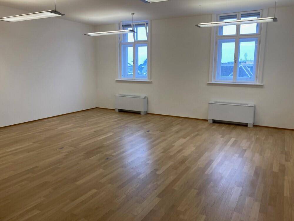 Großes, helles Büro mit Holzboden und drei Fenstern, die viel Tageslicht spenden.
