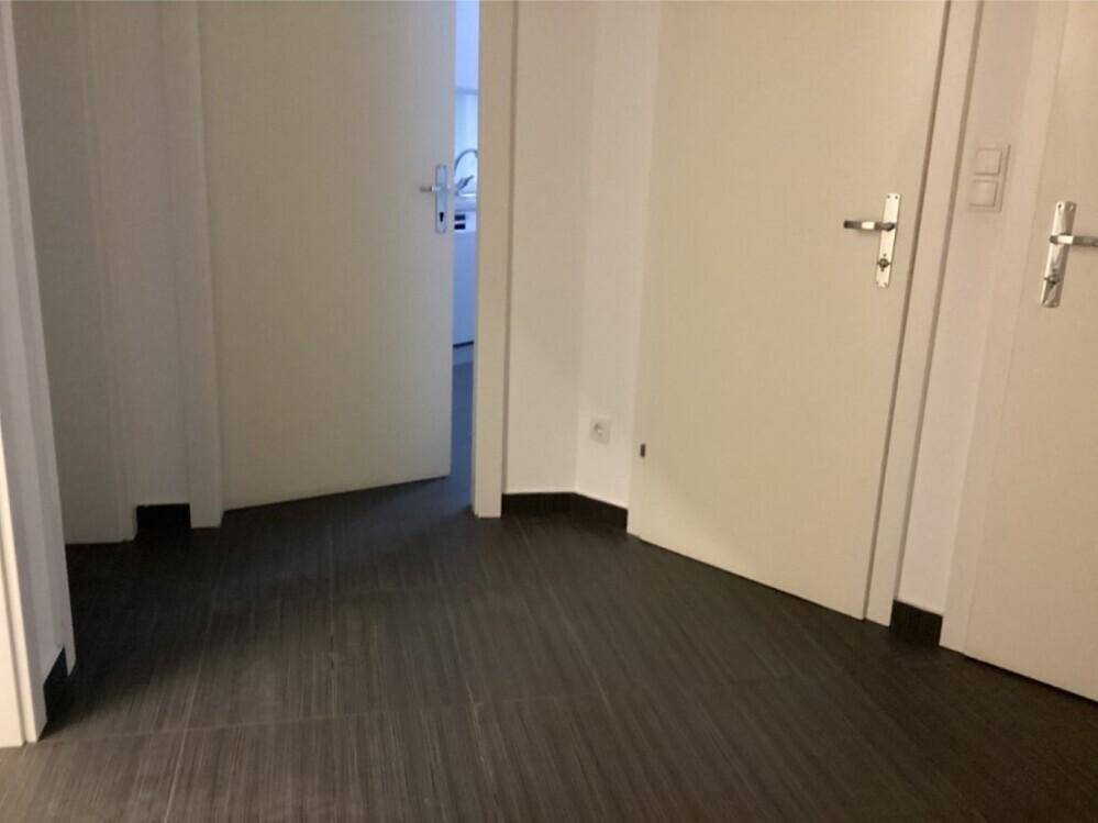Flur mit dunklem Fliesenboden und weißen Türen, der zu weiteren Räumen führt.