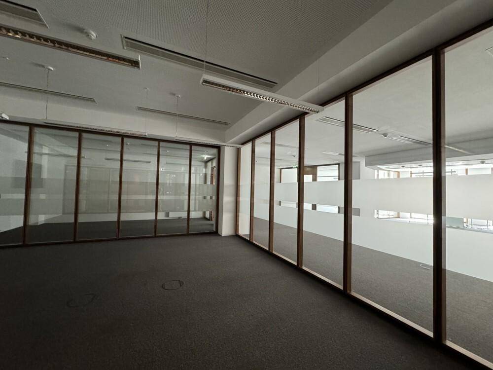 Geräumiges Büro mit Teppichboden und Glaswänden, die separate Arbeitsbereiche schaffen.