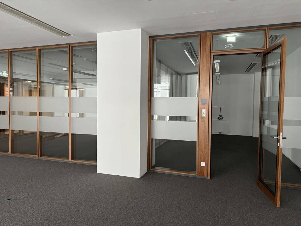 Helles Büro mit Glaswänden und Holztür, die einen separaten Arbeitsbereich abgrenzt.