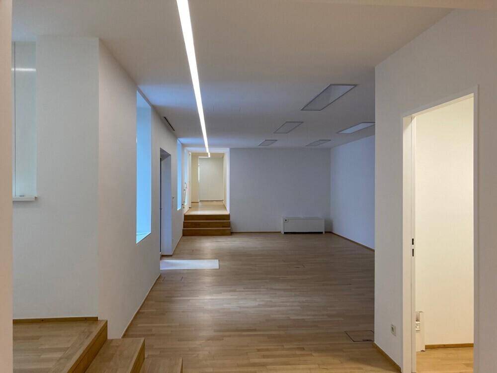 Großzügiger Bürobereich mit Holzboden, Stufen und moderner Deckenbeleuchtung.