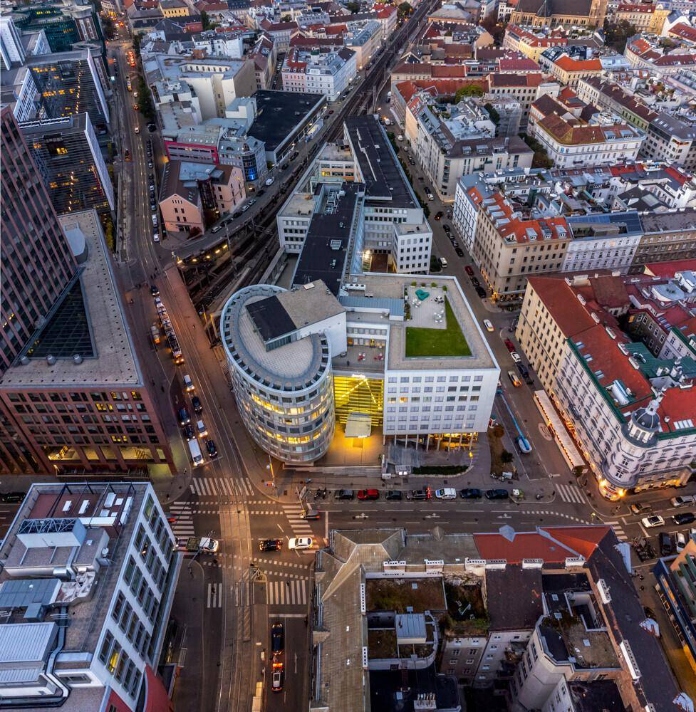Luftaufnahme eines modernen Gebäudekomplexes inmitten einer belebten Stadtlandschaft bei Dämmerung.