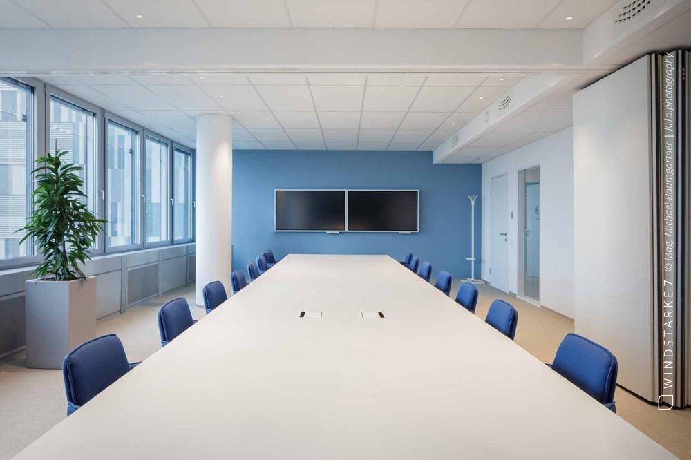 Großer Konferenzraum mit langem Tisch, blauen Stühlen und blauer Akzentwand.