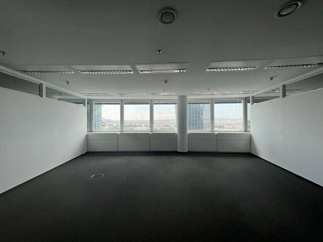Großer, leerer Büroraum mit Teppichboden, breiten Fenstern und einem Panoramablick über die Stadt.