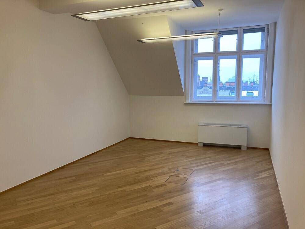 Helles Büro mit Holzboden, Dachschräge und einem großen Fenster mit Stadtblick.