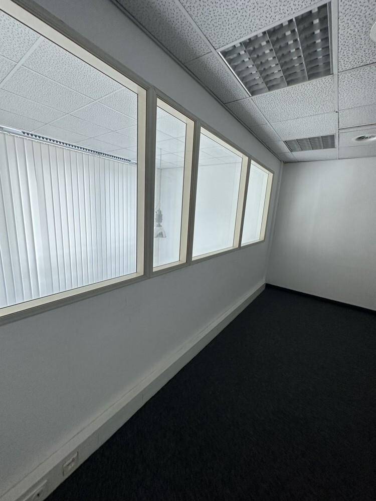 Leerer Büroraum mit dunklem Teppichboden, weißen Wänden und internen Fenstern, die Licht in den Raum lassen.