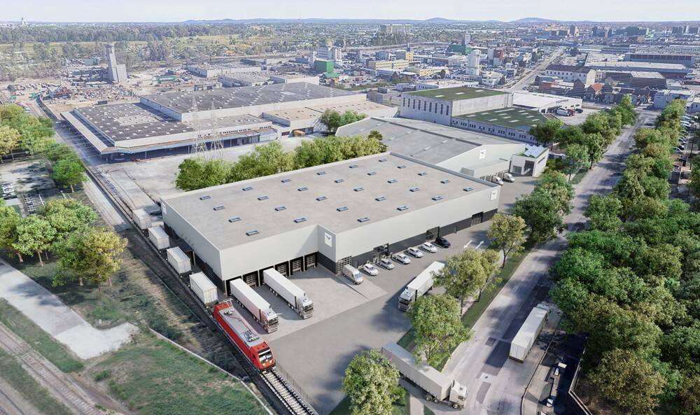 Weitläufige Luftaufnahme eines Logistikzentrums mit Gleisanschluss und LKW-Laderampen in städtischer Umgebung.