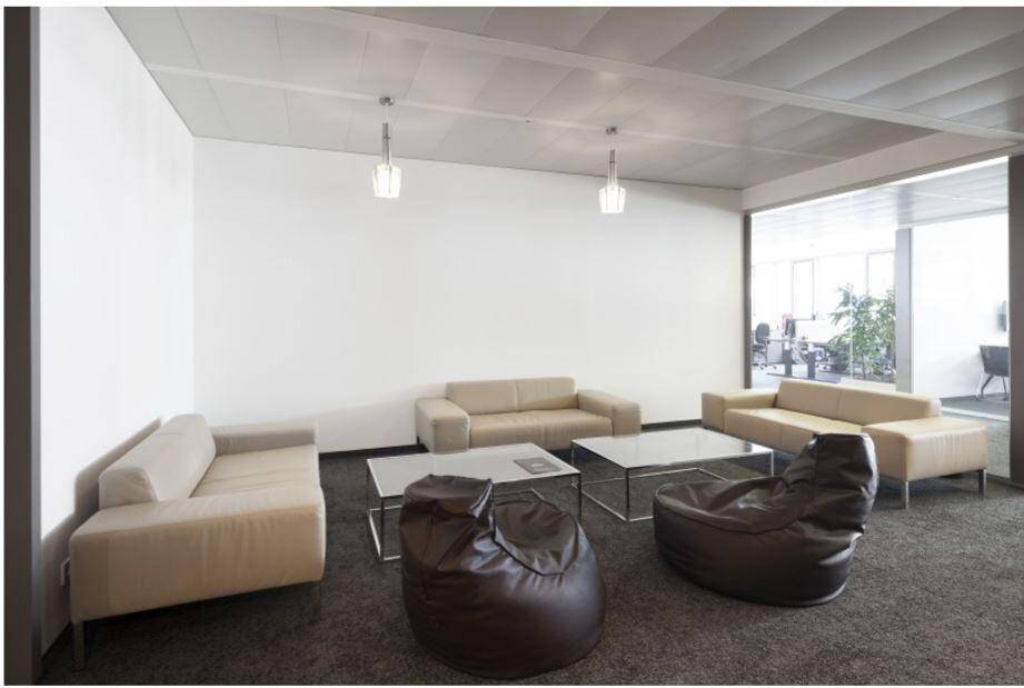 Heller Loungebereich im Büro mit beigen Sofas und großen Fenstern.